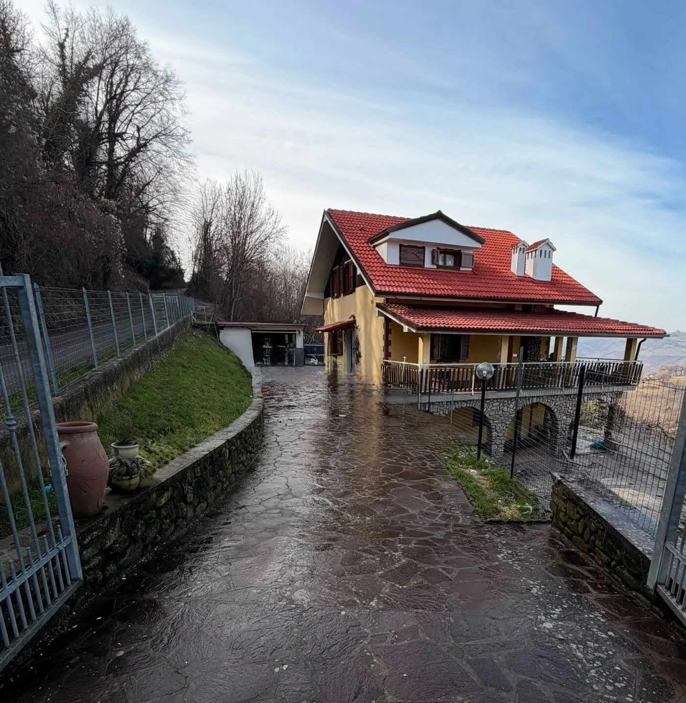 L’ingresso di Kinene a Guiglia: il cancello aperto sul vialetto, la casa con il tetto rosso e la vista sulle colline dell’Appennino modenese